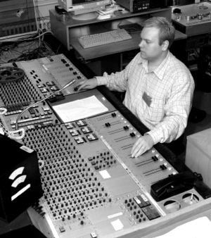 A man sitting at a mixing console with both hands working different areas of the board