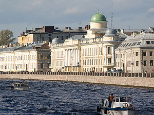 A row of large, stone three-storey buildings alongside a large riverbank